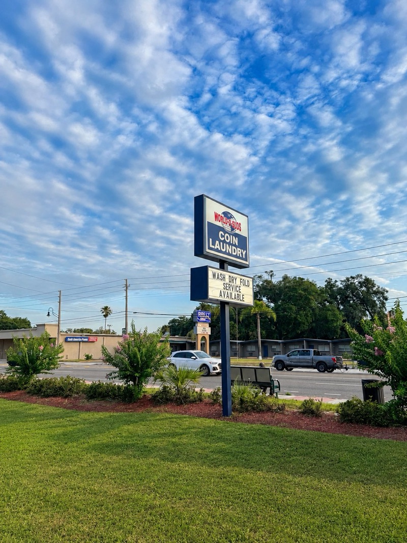 World O' Suds Coin Laundry, 430 E Main St Apopka FL — road sign reading WASH DRY FOLD SERVICE AVAILABLE against a blue sky with clouds